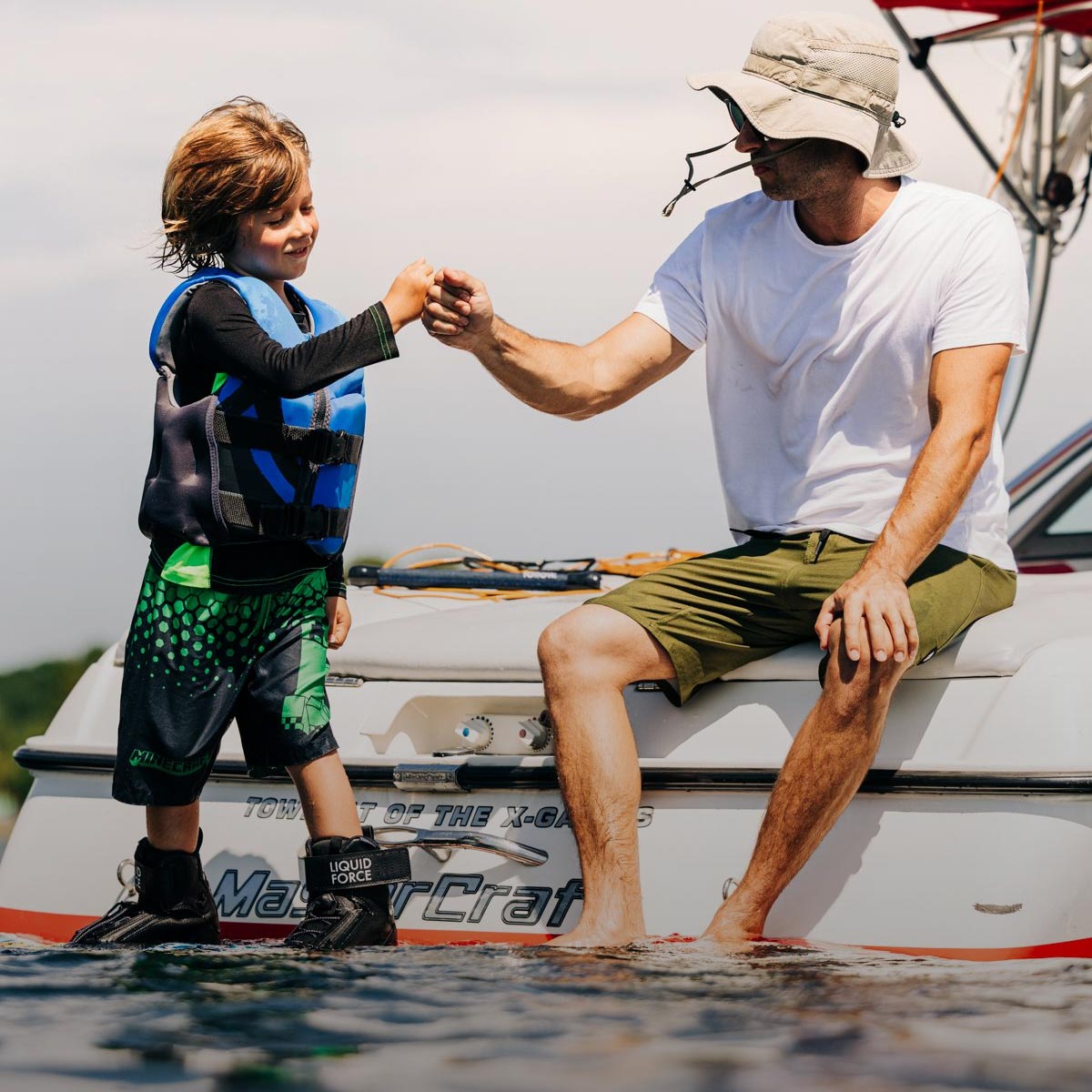 Liquid Force Kid's CGA Vest Collection - Son and father on the back of the boat, where son is in LF Kids CGA getting ready to ride.